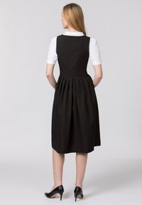 Black dress with a fitted bodice and pleated skirt. White collar with ruffle detail. Worn with black high-heeled shoes. Smooth texture.