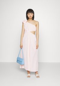 Vestido de um ombro, cor rosa claro, com tecido texturizado, detalhe recortado e acabamento floral. Combinado com uma mala azul e sandálias bege.