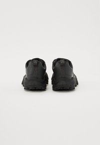 Baskets de sport noires avec un dessus en maille texturée, un talon renforcé et une semelle en caoutchouc durable. Comprend une languette de traction robuste à l'arrière.