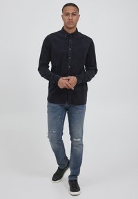 Navy corduroy button-up shirt with a chest pocket, paired with light blue distressed jeans and black sneakers. Slim fit, long sleeves.