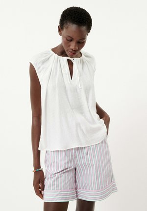 Witte, lichte, korte-mouwen top met een geplooide hals en strikdetail; gecombineerd met gestreepte shorts in roze en groen.