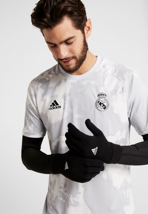 Black knitted gloves with ribbed cuffs. Worn by a person in a gray, speckled adidas shirt featuring a team logo on the chest.