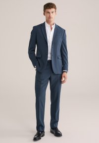 Mörkblå kostym med en figursydd design, enfaldig kavaj och skräddarsydda byxor. Vit skjorta och svarta slipskor fulländar stilen.