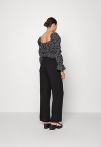 Blusa preta floral com ombros à mostra e mangas bufantes, combinada com calças largas pretas de cintura alta e sandálias chunky.