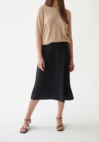 Top beige a maniche corte in maglia abbinato a una gonna midi nera. Tacchi neri con cinturini. Tessuto liscio, design semplice e palette di colori neutri.