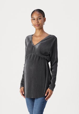 Long-sleeve, grey striped top with a V-neck, designed for maternity wear. Soft texture, accommodating fit around the belly. Paired with blue jeans.
