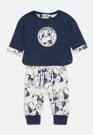 Maglietta a maniche lunghe blu navy con grafica animale, abbinata a pantaloni crema con stampa animale blu. Tessuto di cotone, vestibilità rilassata, polsini a costine.