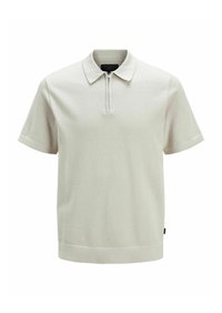 Ljusbeige kortärmad polo med dragkedja i kragen. Tillverkad av texturerad tyg, med rak nederkant och minimal branding.