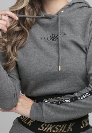 Grijze hoodie met trekkoord en gouden beslag, voorzien van een zwart logo. Band eronder met gouden accenten en merknaam in vetgedrukte letters.