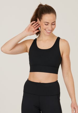 Sort sports-bh med lav scoop-hals, brede stropper og et sømløst design. Lavet af strækbart stof, parret med højtaljede sorte leggings.