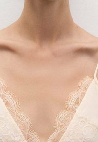 Camisola color crema con detalles de encaje floral delicado en los bordes, ribeteada con encaje y con escote en V y tirantes finos.