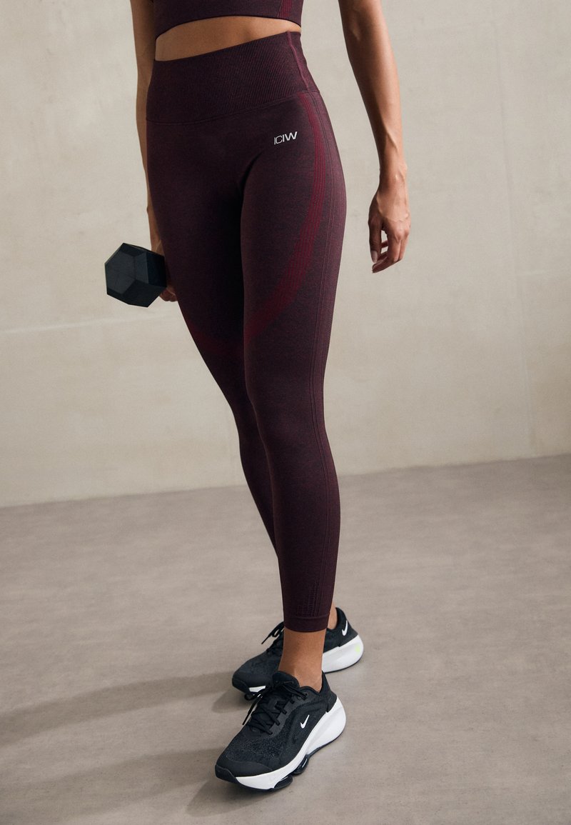 Bordo spalvos treniruočių legginsai su aukštu liemeniu ir subtilia tekstūra, derinami su juodais Nike sportbačiais ir laikant juodą hantelį.