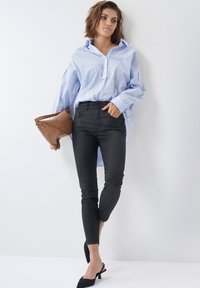 Camisa de botones a rayas azul y blanca, jeans ajustados negros y tacones de slingback negros. Bolsa marrón con diseño curvado. Texturas suaves.