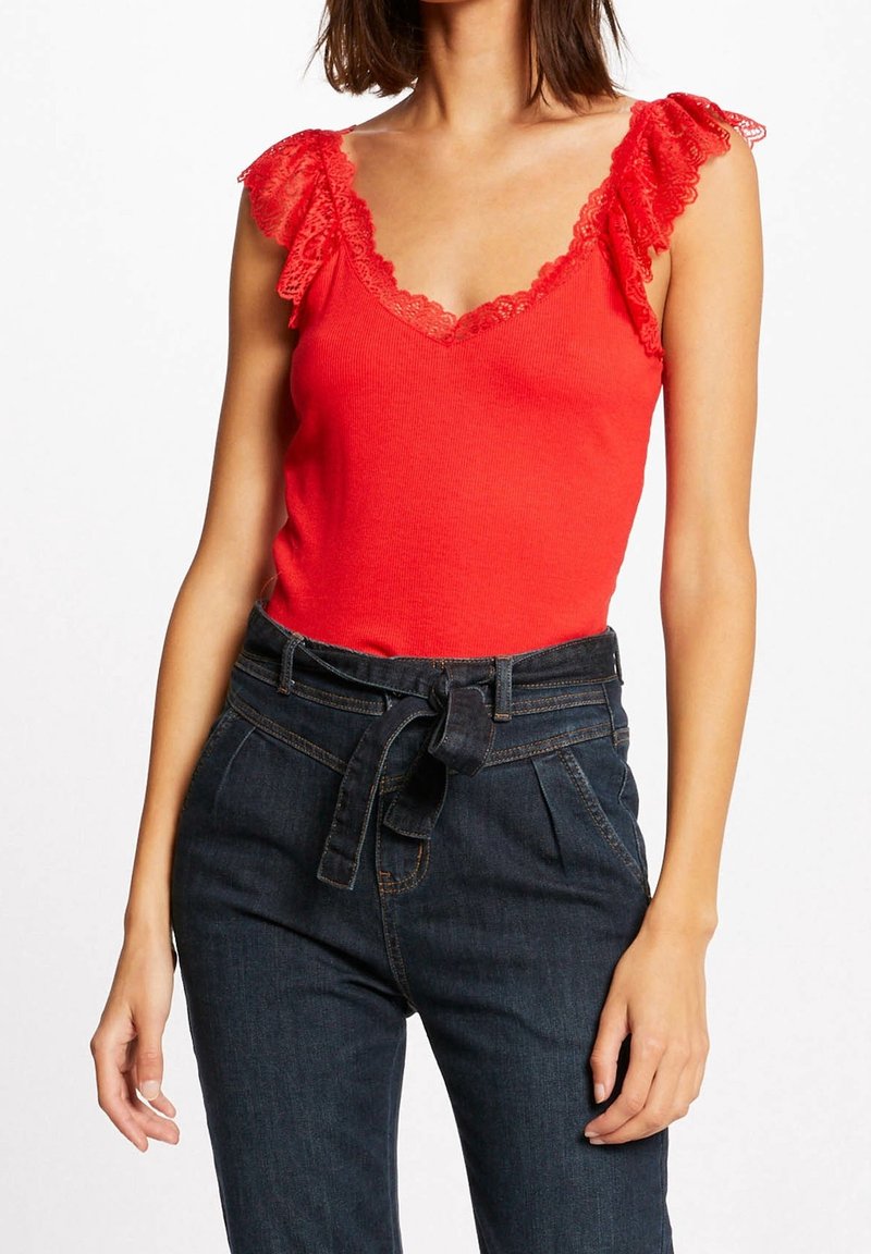 Débardeur rouge côtelé avec bordure en dentelle florale le long de l'encolure et des épaules. Assorti à un pantalon en denim foncé taille haute, orné d'un nœud papillon.