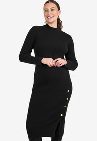 Abito nero a coste con maniche lunghe, collo alto e uno spacco laterale decorato con bottoni dorati, che presenta una silhouette aderente.