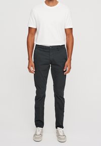 Black cotton chinos with a tapered fit, featuring front pockets, a zip fly, and contrasting stitching, worn with a white crew neck t-shirt.