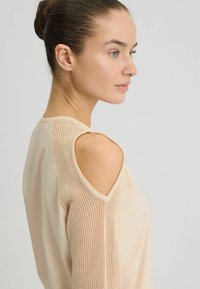 Beige top met uitgesneden schouders, van textuur mesh, gladde stof en een relaxed fit. De halslijn is rond en subtiel.