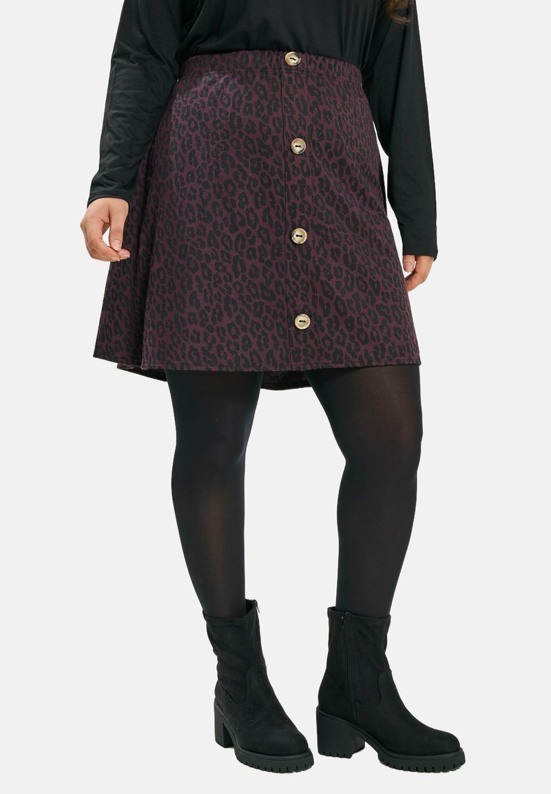 Viininpunainen gepardikuvioinen hame, jossa on liehuva muoto ja kultaiset napit edessä. Yhdistetty mustien sukkahousujen ja nilkkurit kanssa.