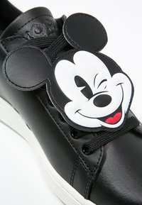 Svart lädersneaker med vit gummisula, med ett stort Mickey Mouse-ansikte som snördekoration och svarta snören.