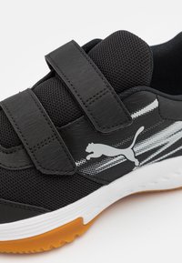 Černá sportovní bota s suchým zipem, síťovinou a gumovou podrážkou. Má bílé logo Puma a šedé pruhované designové akcenty.
