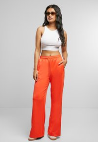 Helle orange Jogginghose mit Kordelzug in der Taille und Seitentaschen, kombiniert mit einem weißen Cropped-Top und Sonnenbrille. Glatte Textur, lässige Passform.