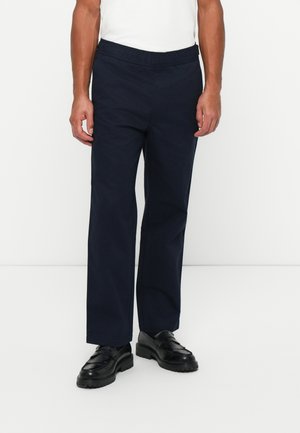 Pantalons bleu marine avec taille élastique, à la coupe décontractée, en tissu lisse. Associés à des mocassins noirs pour un look contrasté.