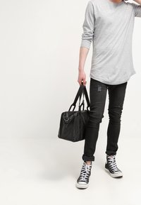 Grå långärmad tröja, svarta slitna jeans, svarta högskor och en svart tote-väska med två handtag bärs.