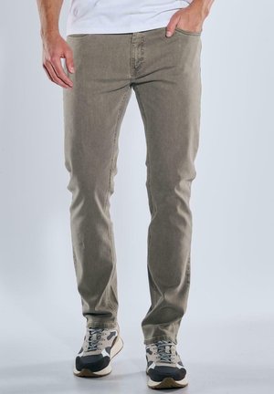 Slim-Fit, hellgrüne Baumwollmischungshose mit fünf Taschen, die eine abgenutzte Textur aufweist. Kombiniert mit grau-schwarzen Sneakers.