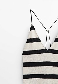 Débardeur en tricot avec un design en V, présentant une base blanche et de larges rayures verticales noires. Bretelles réglables fines et tissu texturé.