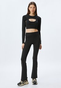 Czarny, długi rękaw crop top z wycięciem z przodu, zestawiony z czarnymi, wysokimi legginsami w dzwony, wykonanymi z elastycznego materiału.