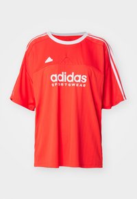 Červený atletický dres s krátkým rukávem, bílými akcenty a logem. Vyroben z hladké tkaniny s vertikálním pruhovaným vzorem a kulatým výstřihem.