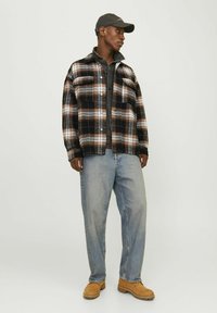 Black and brown plaid flannel shirt with front pockets, worn over a gray shirt, paired with light blue jeans and brown shoes.