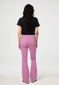 Rode flared jeans met achterzakken en riemlussen, gecombineerd met een zwart shirt met korte mouwen. Gladde stof en aangesloten ontwerp.
