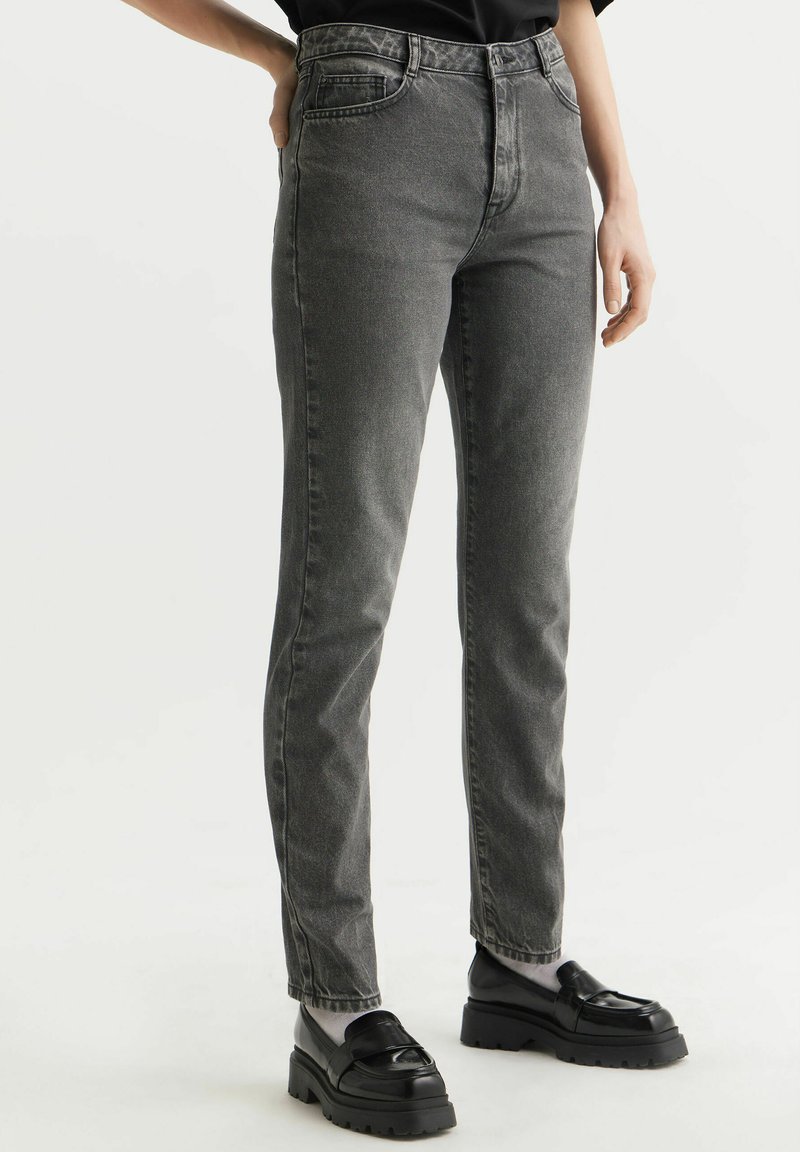 Szare jeansy o wysokim stanie z dopasowaną sylwetką, pięciomaszkowymi kieszeniami, teksturowanym denitem oraz subtelnym, zblakniętym wykończeniem. Połączone z masywnymi, czarnymi loafersami.