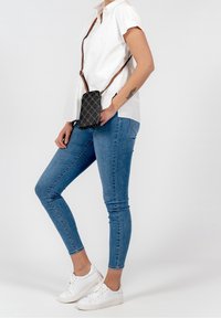 Czarna pikowana torebka z wzorem diamentu, z brązowym regulowanym paskiem. Modelka nosi niebieskie obcisłe dżinsy i białe sneakersy.