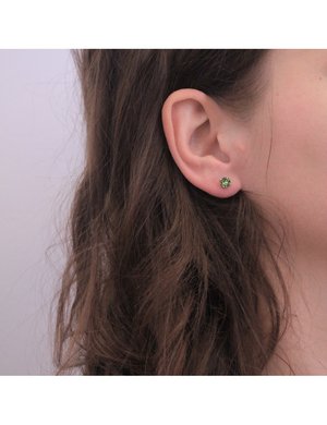 Orecchino a bottone verde rotondo in metallo con una finitura testurizzata, posizionato su un orecchio naturale con capelli castani. Design semplice e minimalista.