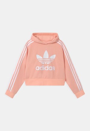 Lys koralrosa cropped hoodie med hvid Adidas trefoil-logo foran og hvide striber ned ad ærmerne, lagt fladt på hvid baggrund.