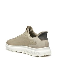 Scarpe da ginnastica beige con una tomaia texturizzata e dettagli in suede, caratterizzate da una suola bianca imbottita con motivi ondulati e un logo sul tallone.