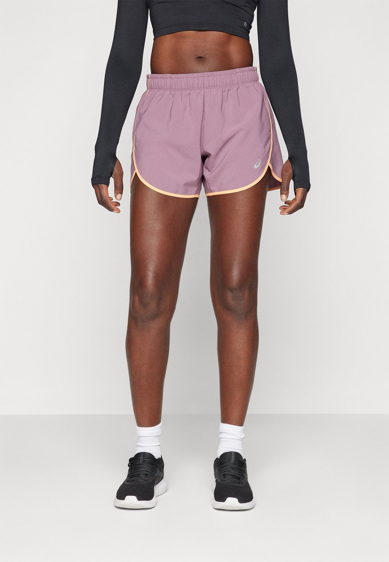 Violet sportiniai šortai su elastinga juosta, kontrastinga geltona apdaila ir logotipo detalė. Modelis dėvi juodas sportines batus su baltais sockais.