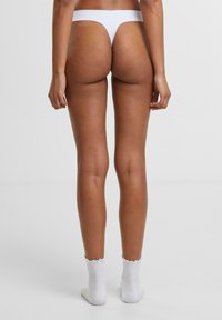 Perizoma bianco mostrato su una persona di spalle, caratterizzato da un design minimalista e una costruzione senza cuciture.