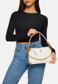 Borsa a tracolla bianca in pelle con dettagli in catena dorata e finiture dorate. Forma rettangolare compatta con un design strutturato e una maniglia superiore.