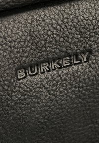 Schwarze Ledertextur mit einem eingeprägten Logo, das "BURKELY" zeigt, und das die Maserung und Details des Materials hervorhebt.