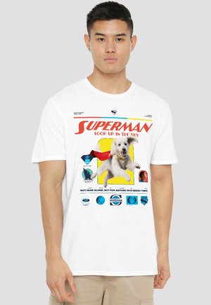 Young man wearing a white t-shirt with a flying dog in a red cape and "Superman Look Up in the Sky" text on the front.