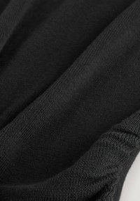 Gros plan sur un tissu noir tricoté montrant une texture détaillée et de fines coutures.