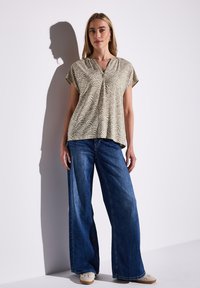 Kortærmet mønster-top i beige med bølgemønster, kombineret med brede blå denimjeans. Outfit er suppleret af lyse sko.