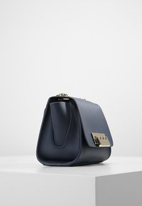 Marinblå läderhandväska med en strukturerad form, utrustad med en guldfärgad metallspänne och detaljerad sömnad. Slät yta med lockstängning.