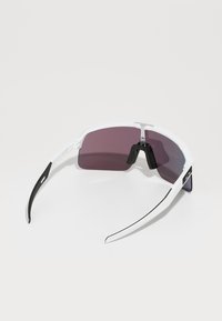 Gafas de sol deportivas con un marco de plástico blanco, lentes de color púrpura oscuro, detalles en negro y un diseño envolvente para una mayor cobertura.