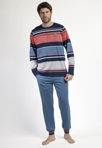 Camisa de manga larga a rayas en rojo, azul marino y gris con cuello redondo; combinada con pantalones de chándal azul con puños acanalados.
