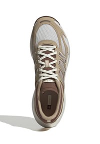 Gornji pogled na bež i smeđi atletski tenisica s bijelim vezicama, mrežastim gornjim dijelom i jastučićem oko ankl, koji baca sjenu na bijelu pozadinu.