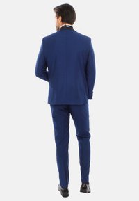Completo blu da uomo con vestibilità su misura, realizzato in tessuto liscio. Presenta uno spacco singolo, pantaloni slim e scarpe eleganti nere lucide.